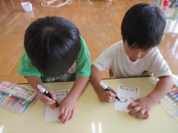 ハガキに祖父母の顔の絵を描いている子供