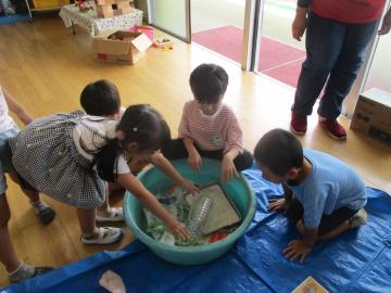 牛乳パックをタライの中の水に浸す子供たち