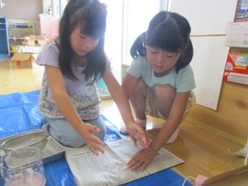 新聞紙で牛乳パックをはさんで水気をきる子供たち