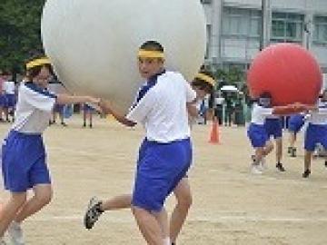 3人で手をつなぎ大玉を運ぶ生徒