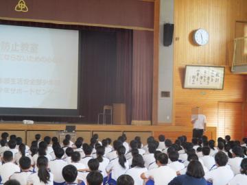 舞台上のプロジェクターの前で講師の方が話をしている様子を三年生が真剣に聞いています。