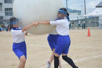 三人の生徒が手をつないで、白色の大玉を運んでいます。