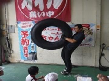 大きなタイヤを持ち上げるお店の方の写真