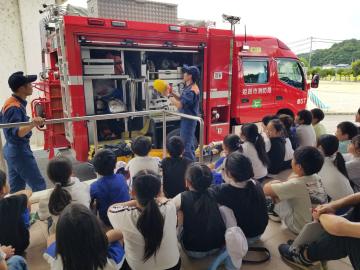 消防車の前で消防局職員の方の説明を聞いている3年生の児童たちの様子