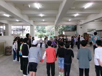 建物内で5年生が輪になって歌を歌っている様子