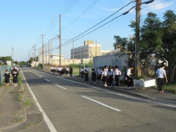 大的街道沿いの歩道を東から西へ歩いてごみ拾いをする生徒たちの様子