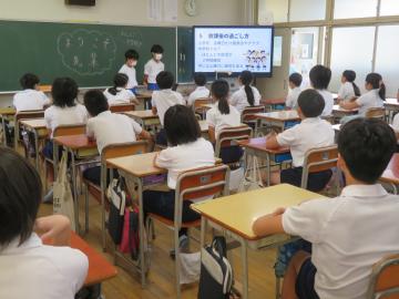 教室内でモニターを活用して説明する中学生の発表を静かに聞く6年生の様子