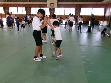 9年生が1年生に竹馬を教えている様子