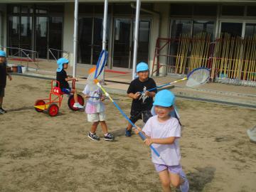 園庭で虫網を使ってトンボを追う園児たちの様子