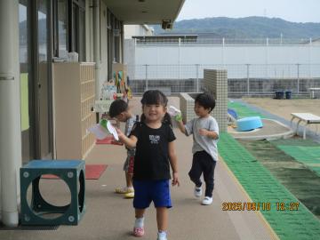 園庭前の廊下で手作りトンボを使って遊んでいる園児たちの様子