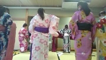 艶やかな浴衣を着て帯を締めようと頑張る女子生徒たち