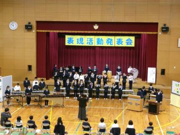 体育館の壇上で、3年生から6年生の児童たちが頑張って演奏している様子