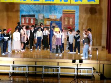 体育館の壇上で、5年生と6年生がみんなで演技している様子