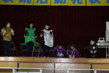体育館の壇上で、3年生と4年生の児童たちがおばけになりきって演技している様子