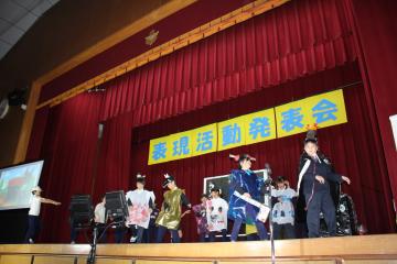 体育館の壇上で、3年生と4年生の児童たちがたくさんのおばけの演技をしている様子