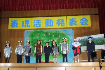 体育館の壇上で、1年生と2年生の児童たちがそろって最後の演技をする様子