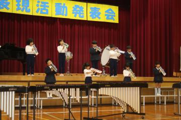 体育館の壇上で児童たちが鍵盤ハーモニカを演奏している様子