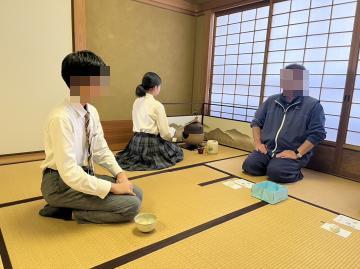 作法室で、茶道部員と教師が向かい合い、お茶を振舞っている様子