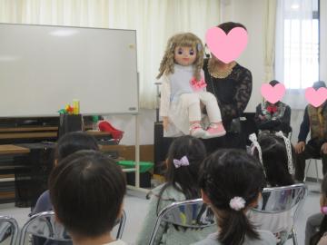 室内で人形を手に持ち、子供たちに向けて腹話術をする女性の様子