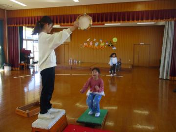 遊戯室で上空のタンブリンを目掛けて踏み台でジャンプをする園児たちの様子