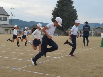 校庭のトラック上で中学年の児童が徒競走でゴールする様子