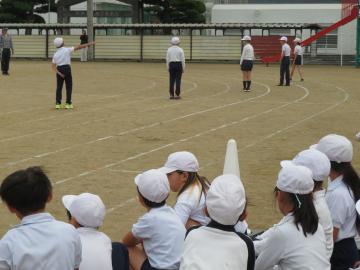 校庭のトラック上で中学年の児童が徒競走で選手紹介されている様子