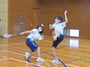 体育館でバトミントンの試合をしていて、ラケットを振りかぶっている生徒2人