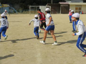 校庭でコーチからボールを奪おうとする児童たちの様子