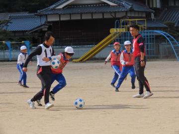 校庭でコーチと競り合う児童たちの様子