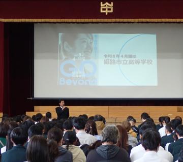 体育館で進路説明会が開催され、壇上の表示を観ながら説明を聴く生徒たちの様子