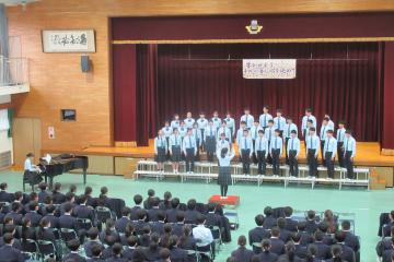 体育館の壇上で、9年1組の生徒が合唱をしている様子