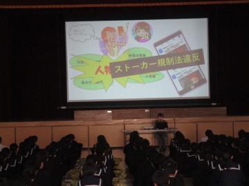 体育館で全校生徒がプロジェクターに表示された画面で講義を聴いている様子