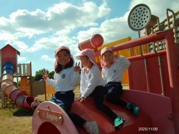 公園内の遊具の上にまたがって笑顔を向ける園児たちの様子