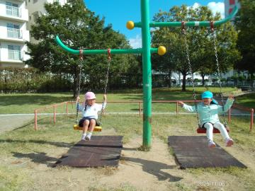 公園内で二人並んでブランコを漕ぐ園児たちの様子