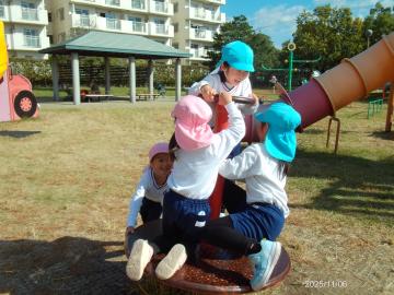 公園内で回転する遊具にしがみついて楽しむ園児たちの様子