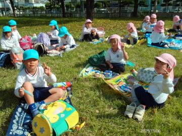 公園内の芝生の上にシートを敷いて弁当を食べる園児たちの様子