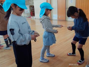 室内で小学生がこまのひもの巻き方を幼児に教えている園児たちの様子