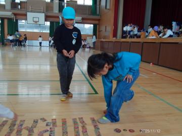 体育館内で、めんこを投げようとする幼児とめんこを並べる小学生の様子