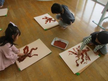 室内でローラーを使い柿の木の幹や枝を描く園児たちの様子