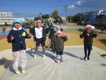 園庭で大きなトランポリンの上でこちらを向いて飛び跳ねる園児たちの様子