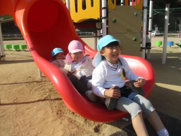 公園内のすべりだいから3人の子供が連なって滑り降りてきている園児たちの様子