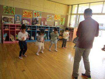 遊戯室内で講師に教わり、膝を曲げた姿勢でけん玉に取り組む園児たちの様子