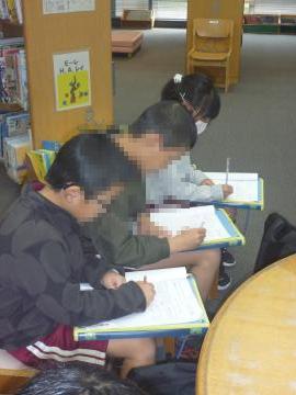 図書館内で説明を聞いてメモを取る児童の様子