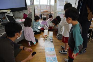 風の力で進む車を教室の床で走らせる児童たち