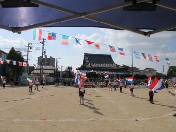 運動場に等間隔に整列した園児たちがカラーガード演技をしています。