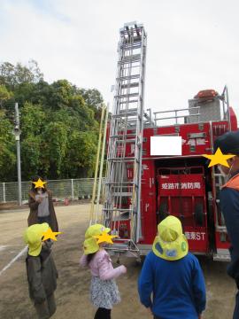消防車から伸びるはしごを見上げる園児