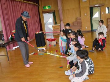 広場に座った園児たちがマジックショーを見て参加しているようす