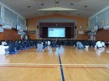 体育館でスライドを見ながら講師の方のお話を聞く生徒たちの様子