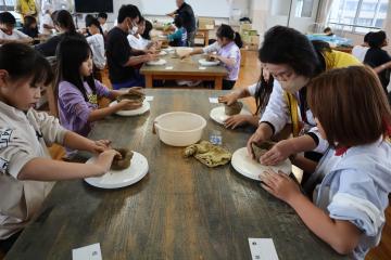 テーブルに座って子どもたちがお皿等を土で作っています