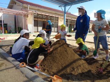 中学生のお姉さんと一緒に砂場で山を作っている